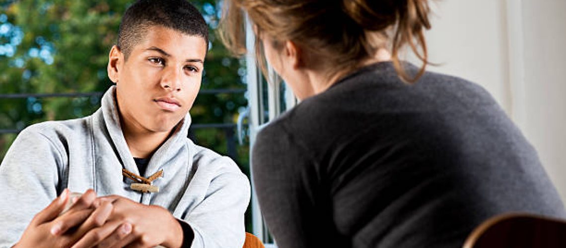 Female counsellor or teacher talking to a mixed race male teenager.